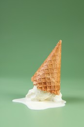 Photo of Melted ice cream and wafer cone on green background, space for text