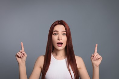 Photo of Surprised woman with red dyed hair pointing upwards on light gray background