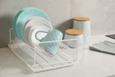 Drainer with different clean dishware and cup on light table indoors