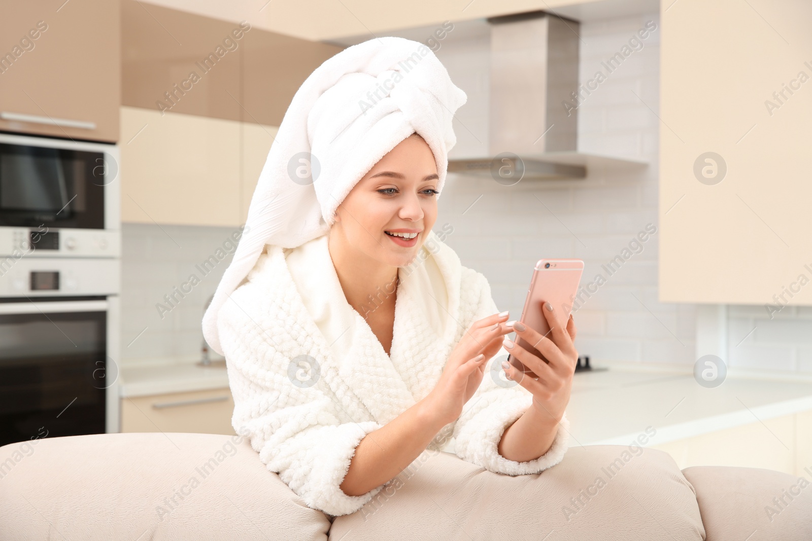 Photo of Beautiful woman with hair wrapped in towel using smartphone at home