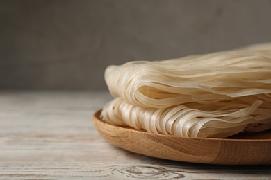 Photo of Plate with raw rice noodles on wooden table, closeup. Space for text
