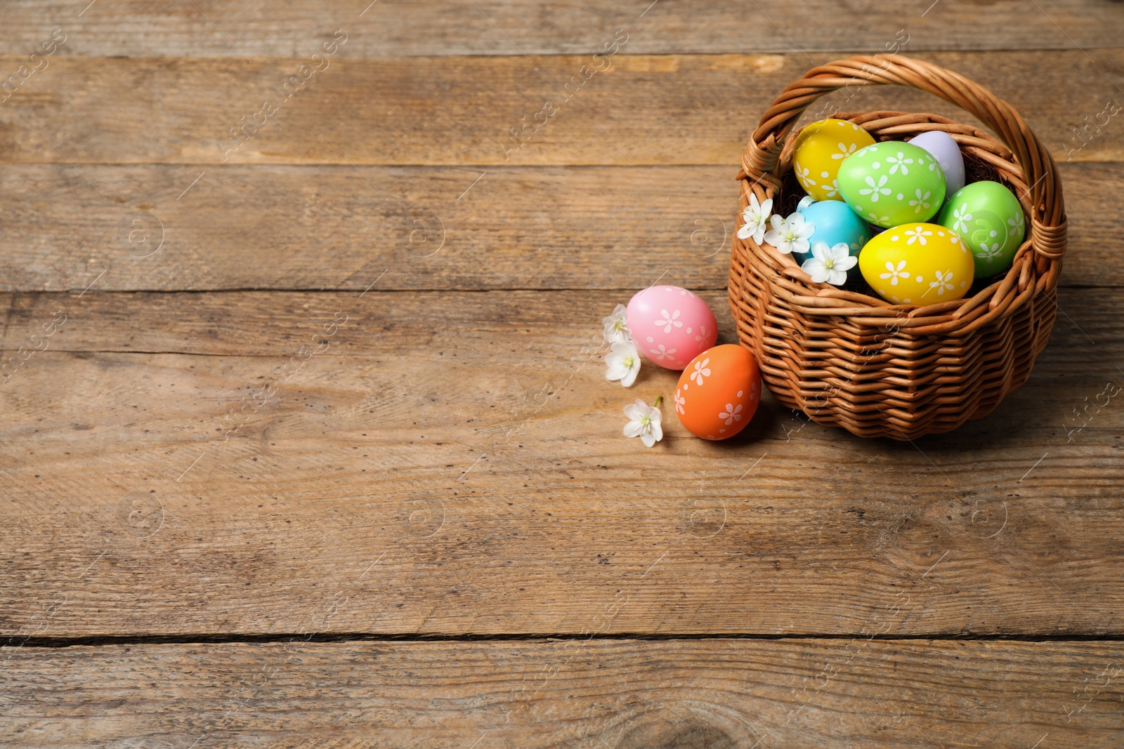 Photo of Colorful Easter eggs in basket and flowers on wooden background. Space for text