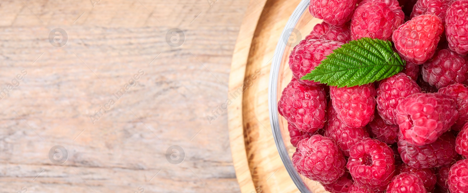 Photo of Delicious fresh ripe raspberries in bowl on wooden table, top view. Space for text