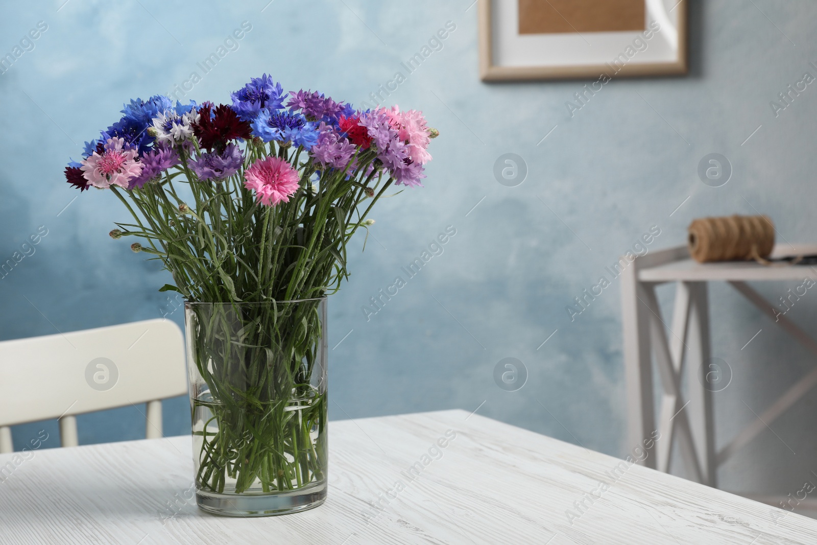 Photo of Bouquet of beautiful cornflowers in glass vase on white wooden table at home. Space for text