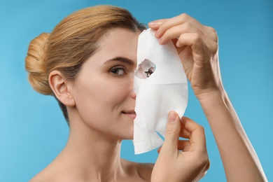 Photo of Beautiful woman with cotton facial mask sheet against color background