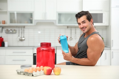 Young athletic man with ingredients for protein shake in kitchen, space for text