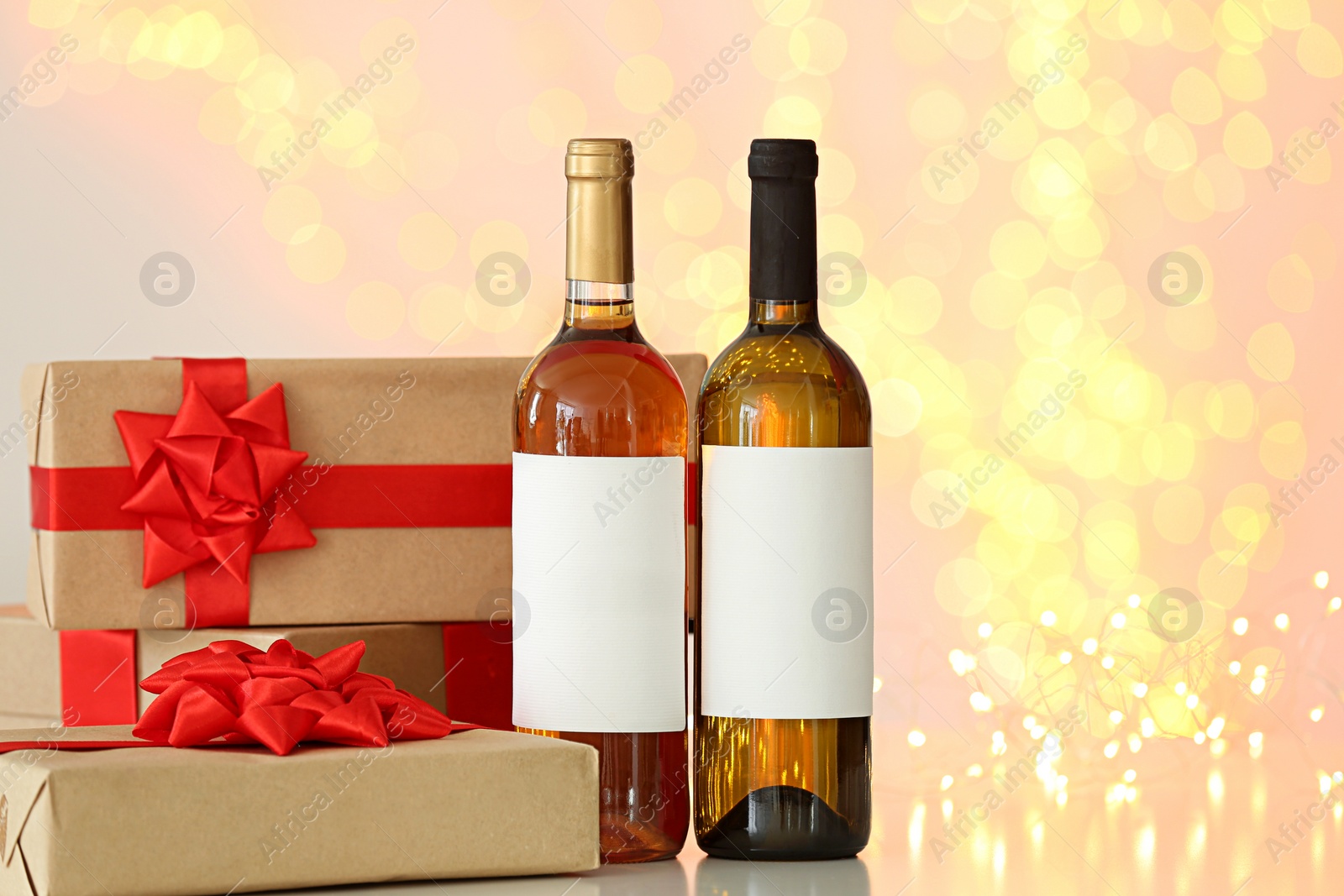 Photo of Bottles of wine and gift boxes on table against blurred lights. Space for text