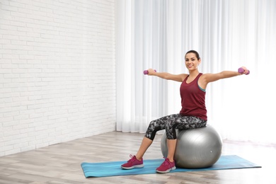 Photo of Young beautiful woman with ball doing exercise at home, space for text. Workout and fitness