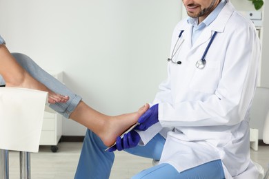 Photo of Male orthopedist fitting insole to patient's foot in hospital, closeup