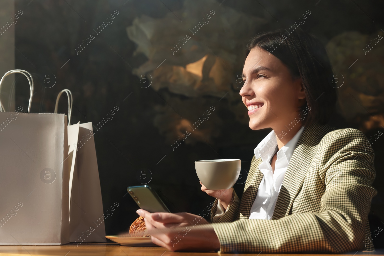 Photo of Special Promotion. Happy young woman with cup of drink using smartphone at table in cafe