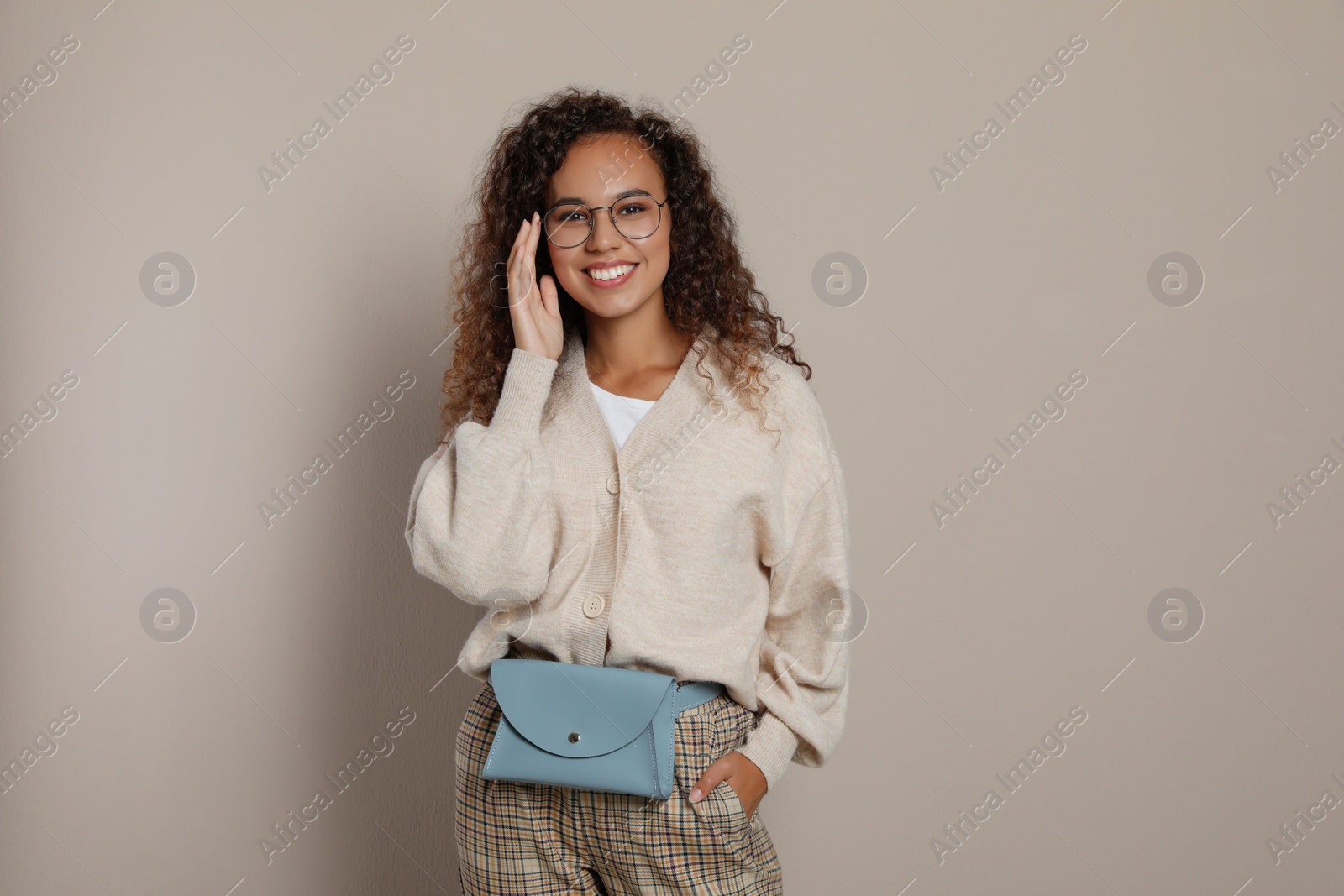 Photo of Beautiful African American woman with stylish waist bag on beige background