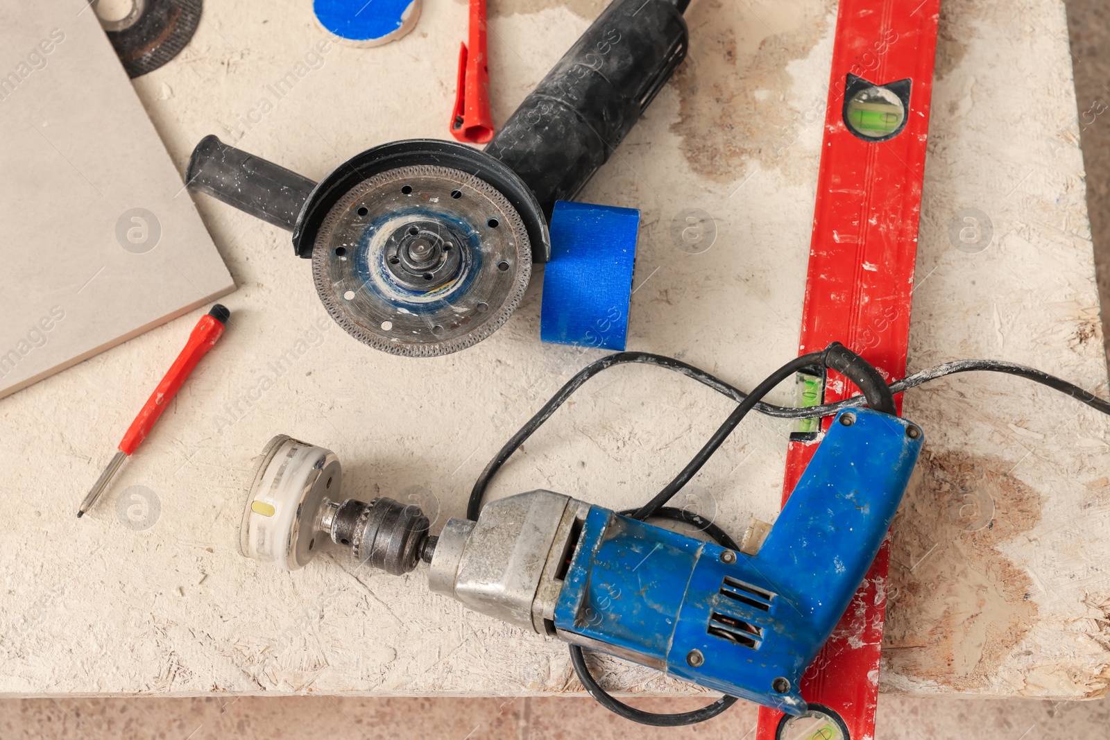 Photo of Buffing attachment drill and saw on chipboard indoors. Tiles installation process