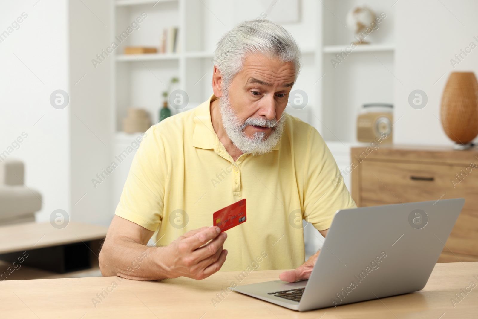 Photo of Stressful senior man with credit card using laptop at home. Be careful - fraud