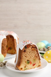 Piece of glazed Easter cake with sprinkles and candied fruits on white wooden table
