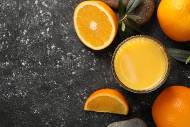 Photo of Tasty fresh oranges, juice, stones and leaves on black table, flat lay. Space for text