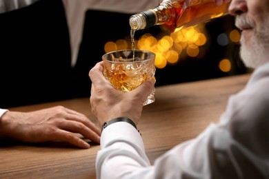 Bartender pouring whiskey in glass for customer at bar counter, closeup