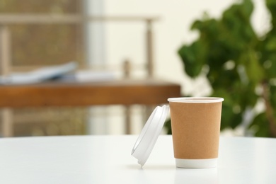 Photo of Cardboard cup of coffee on table indoors. Space for text