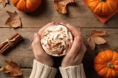 Woman holding tasty pumpkin latte at wooden table, top view