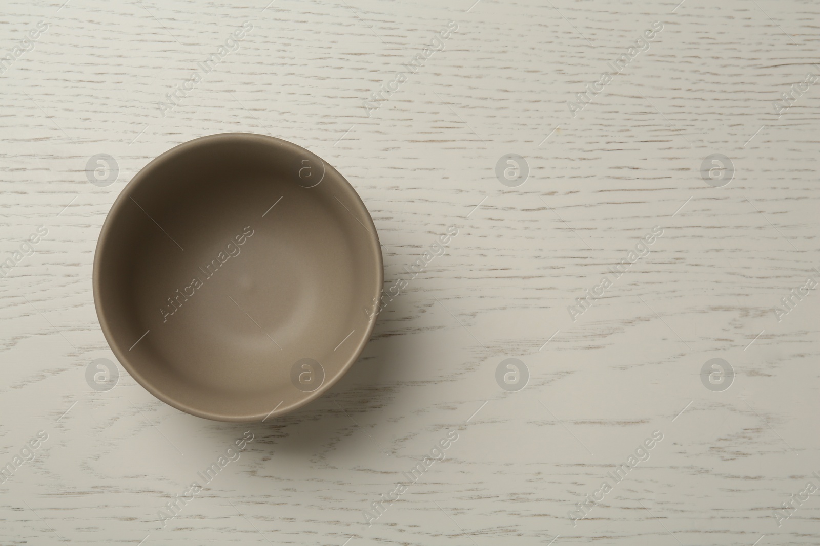 Photo of Stylish empty ceramic bowl on white wooden table, top view and space for text. Cooking utensil