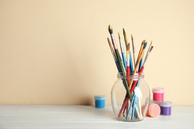 Glass with brushes and paint jars on table against color background. Space for text