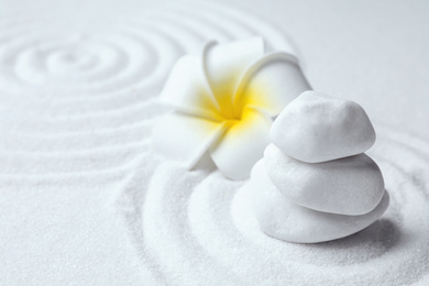 Stack of white stones and beautiful flower on sand with pattern. Zen, meditation, harmony