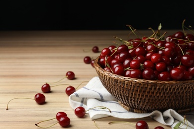 Photo of Wicker bowl of delicious cherries with towel on wooden table, space for text