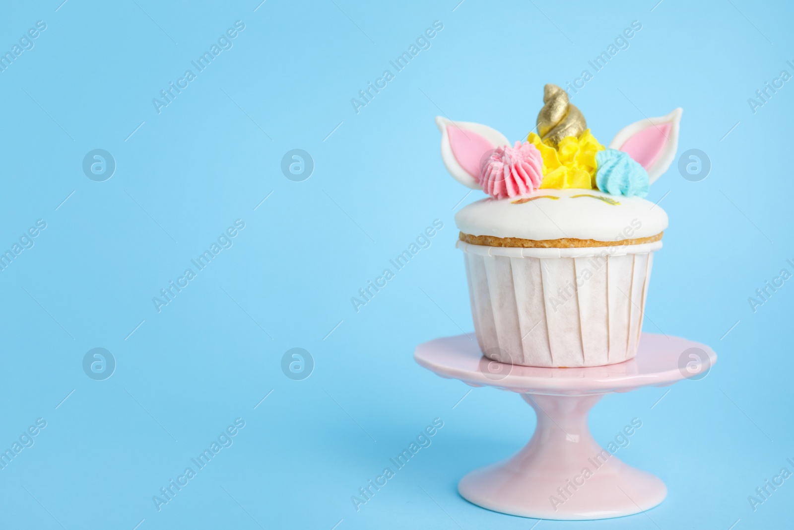 Photo of Dessert stand with cute sweet unicorn cupcake on light blue background. Space for text