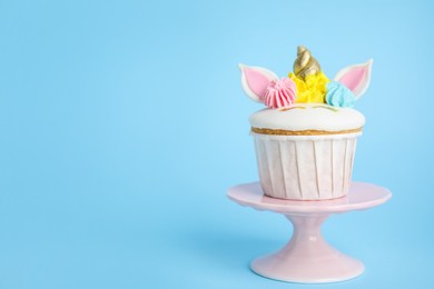 Photo of Dessert stand with cute sweet unicorn cupcake on light blue background. Space for text