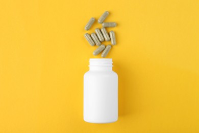 Photo of Bottle and vitamin capsules on yellow background, top view