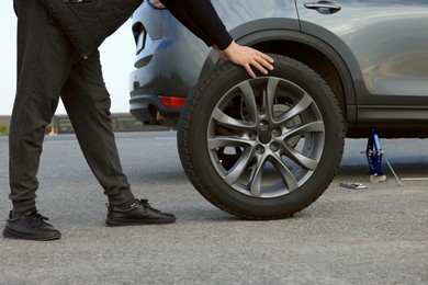 Photo of Man changing tire of car on roadside, closeup