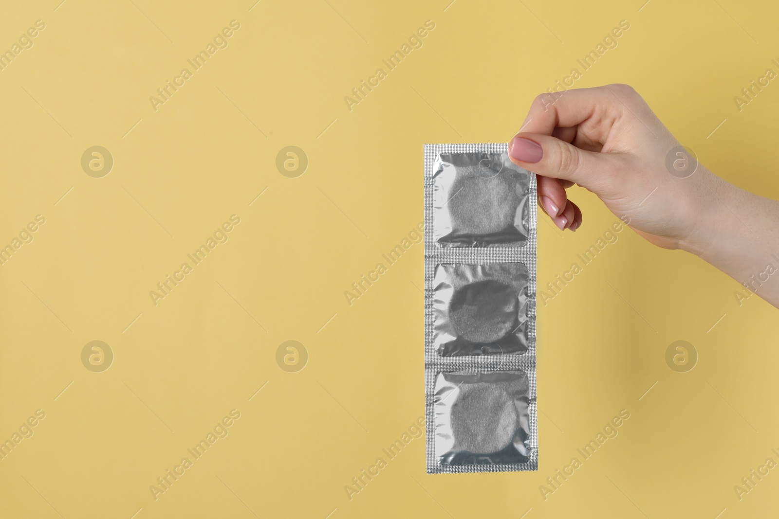 Photo of Woman holding condoms on pale yellow background, closeup. Space for text