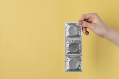 Photo of Woman holding condoms on pale yellow background, closeup. Space for text