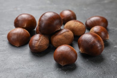 Photo of Roasted edible sweet chestnuts on grey textured table, closeup