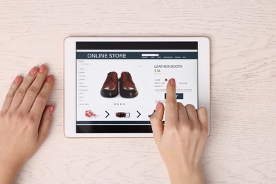 Woman with tablet shopping online at white wooden table, top view