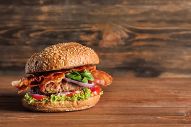 Photo of Tasty burger with bacon on wooden table