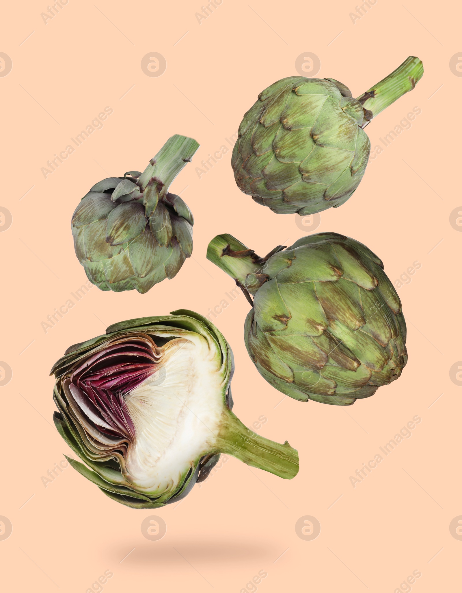 Image of Fresh raw artichokes falling on pale orange background