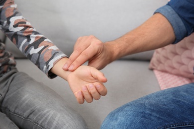 Man checking little boy's pulse with fingers indoors, closeup