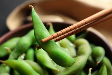 Photo of Bowl with green edamame beans in pods and chopsticks, closeup
