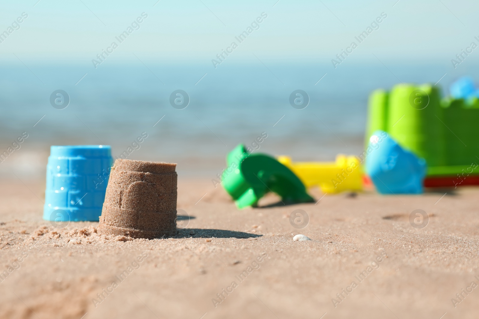 Photo of Different child plastic toys and sand castle on beach. Space for text