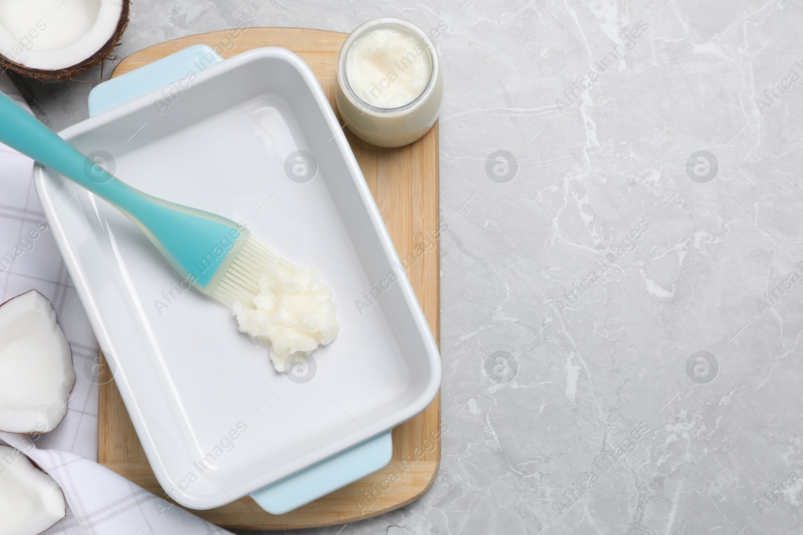 Photo of Baking dish with coconut oil and silicone brush on light grey table, flat lay. Space for text