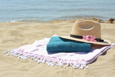 Photo of Blanket with towel, stylish straw hat and flowers on sand near sea, space for text. Beach accessories