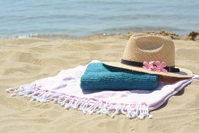 Blanket with towel, stylish straw hat and flowers on sand near sea, space for text. Beach accessories