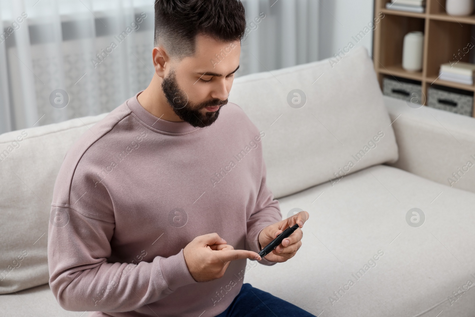 Photo of Diabetes test. Man checking blood sugar level with lancet pen on sofa at home