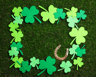 Frame made of clover leaves and horseshoe on grass, space for text. St. Patrick's Day celebration