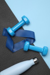 Photo of Two dumbbells, yoga mat, fitness elastic band and thermo bottle on light blue background, flat lay