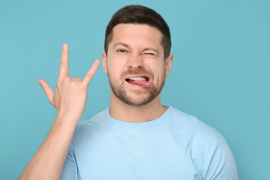 Man showing his tongue and rock gesture on light blue background