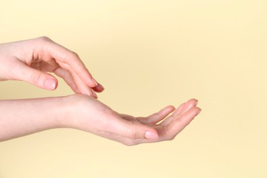 Woman applying cream on her hand against yellow background, closeup