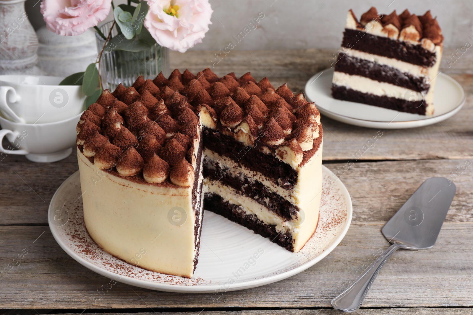 Photo of Delicious tiramisu cake with cocoa powder on wooden table