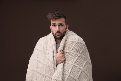 Photo of Man wrapped in blanket suffering from fever on brown background. Cold symptoms