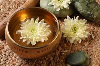 Photo of Tibetan singing bowl with water, beautiful chrysanthemum flowers, mallet and stones on table, closeup